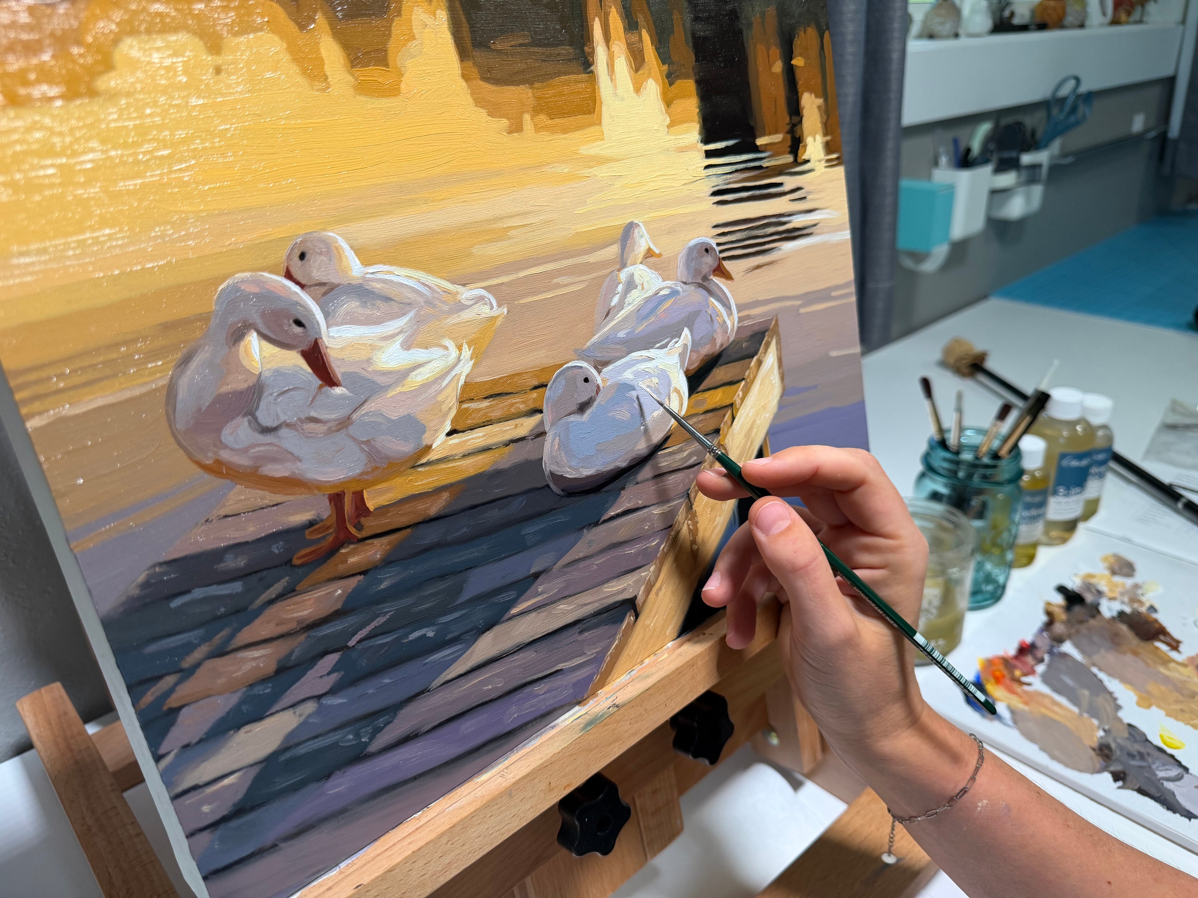 Artist Lauren Pretorius painting ducks on a canvas with a brush, surrounded by art supplies.