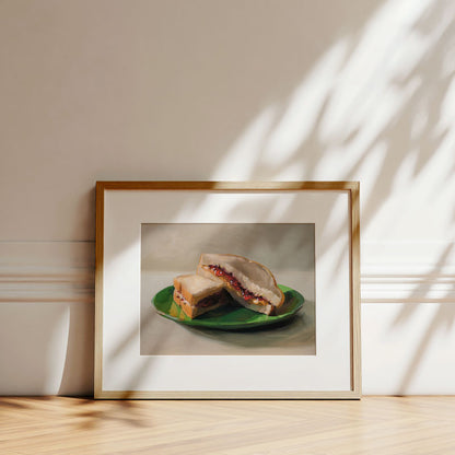 Fine art print of a peanut butter and jelly sandwich on a green plate, displayed in a light wood frame on a floor.