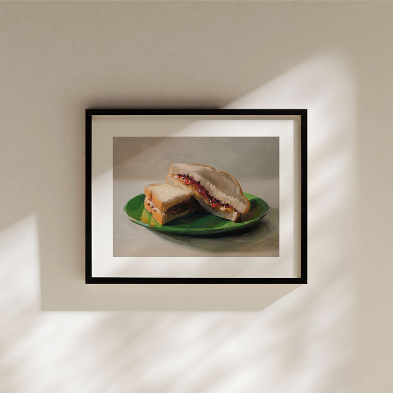 Fine art print of a peanut butter and jelly sandwich on a green plate, framed in black with a white mat border.