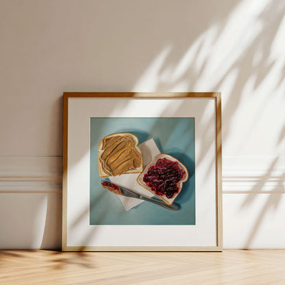 Framed fine art print of a peanut butter and jelly sandwich on a napkin, displayed in a light wood frame on a floor.