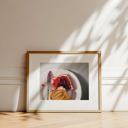 Framed fine art print of a peanut butter and jelly sandwich on a plate, displayed against a wall with soft leaf shadows.