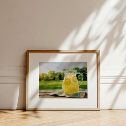 Framed fine art print of a lemonade pitcher on a wooden table, featuring a sunny garden background and soft leaf shadows.