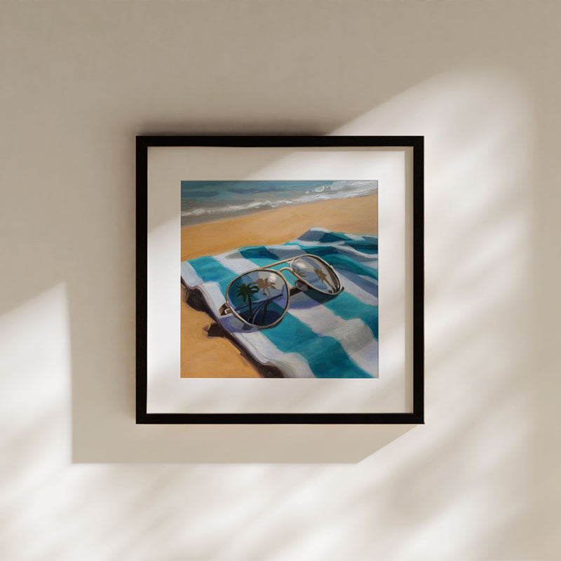 Fine art print of sunglasses on a blue and white striped beach towel, framed in black on a neutral wall.