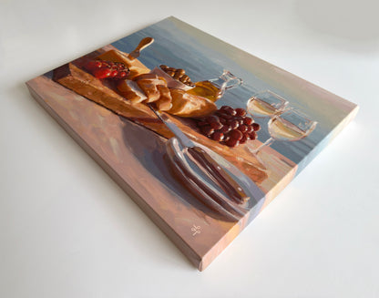 A square canvas painting depicting a still life scene with bread, grapes, a bottle, and two wine glasses on a wooden board, photographed at an angle on a clean white background.