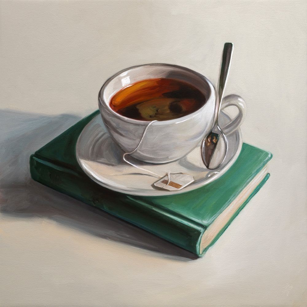 Teacup with saucer and spoon on a green book against a neutral background