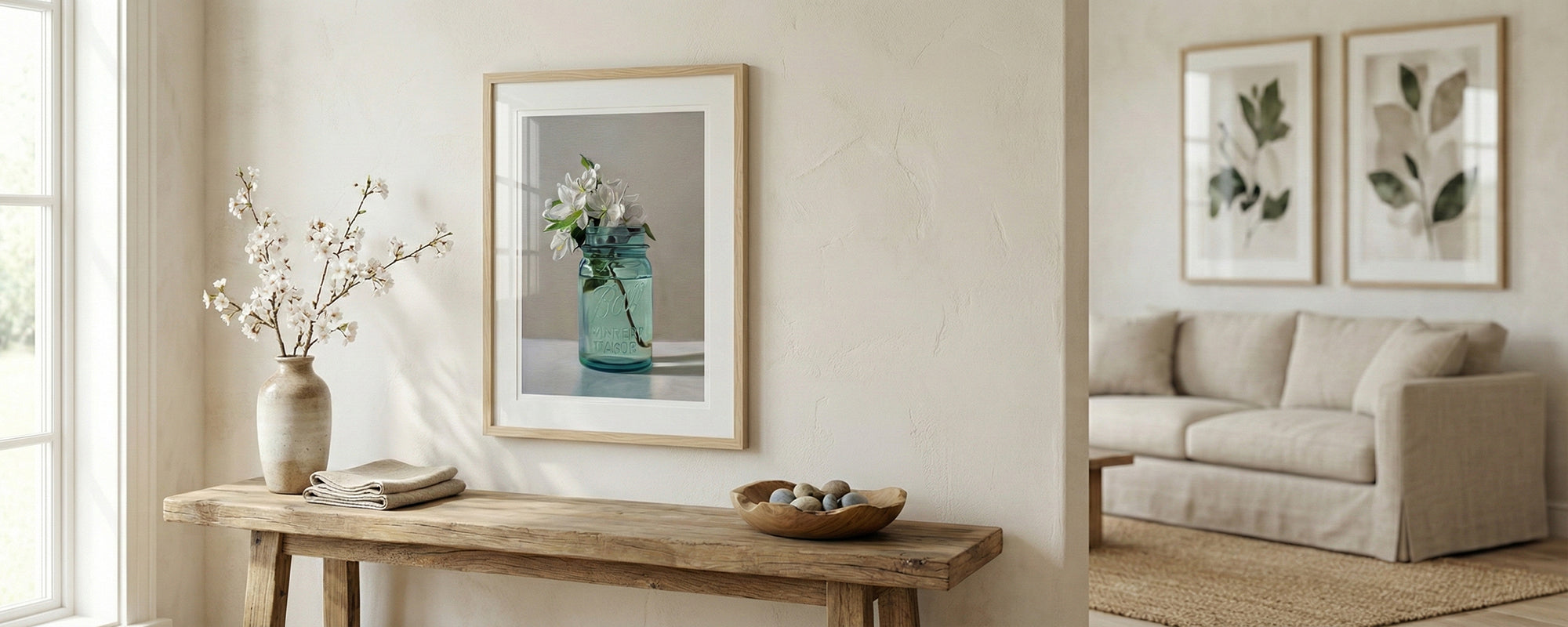 Living room with a wooden console table, framed artwork by Lauren Pretorius featuring white flowers in a turquoise jar, and a beige sofa.