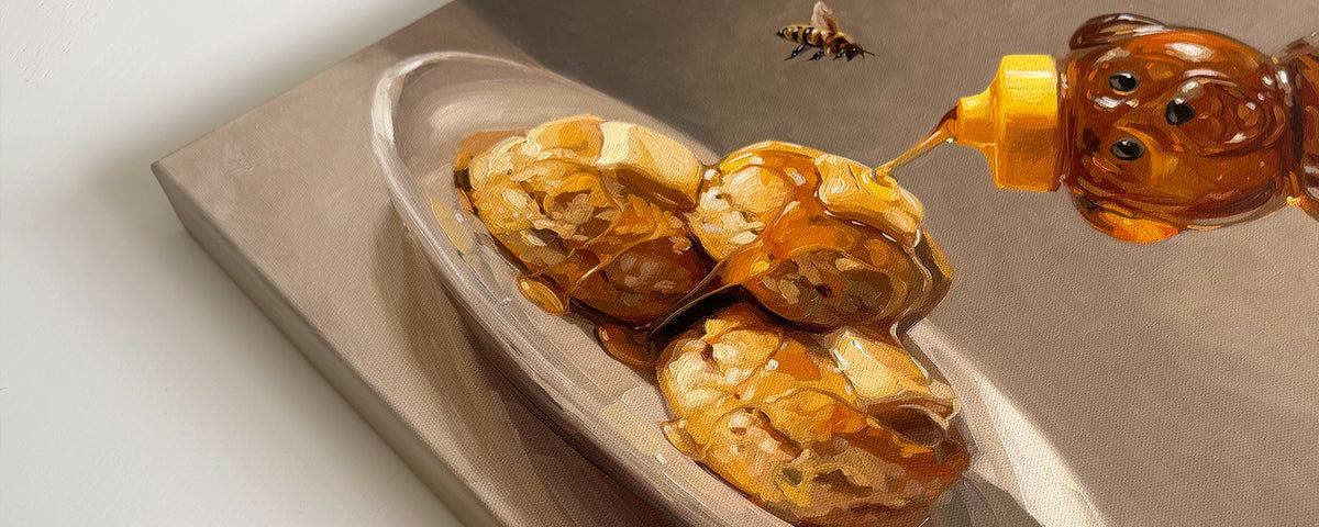 A painting of three golden-brown biscuits on a plate, being drizzled with amber honey from a bear-shaped honey bottle. A small bee is visible in the upper right against a neutral studio background.