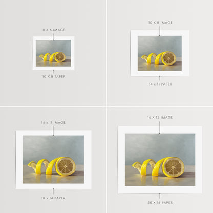 Lemon Twist Fine Art Print by Lauren Pretorius: a lemon half with its peeling spiraling out towards the left on a light, reflective surface and muted blue background.