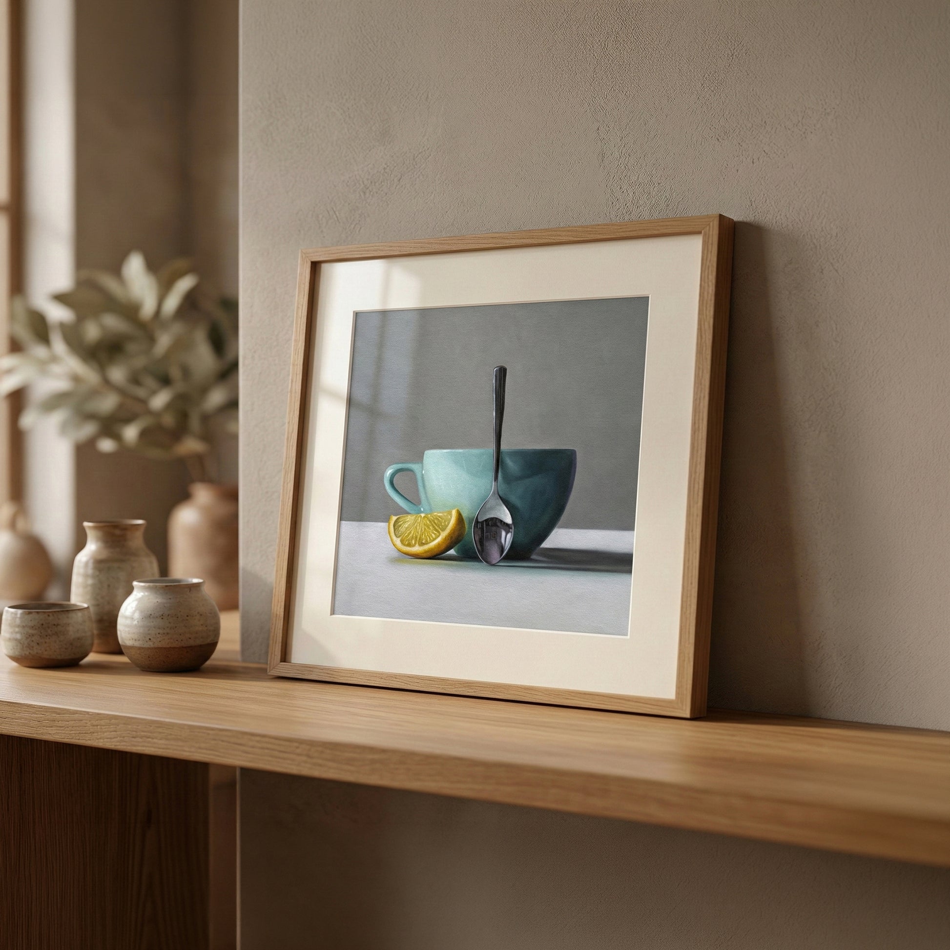 Framed fine art print of a lemon wedge, teal cup, and spoon, displayed on a wooden shelf.