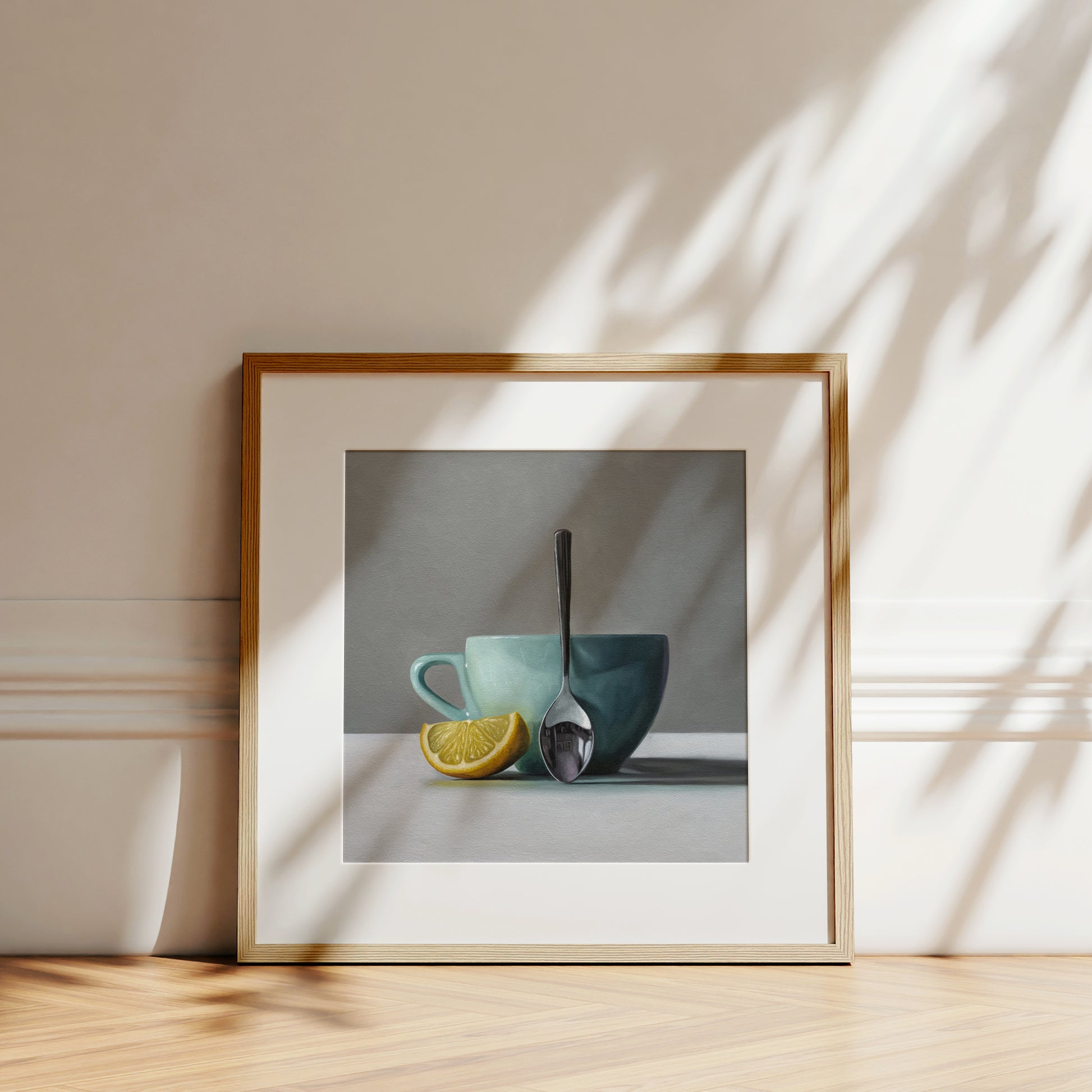 Framed fine art print of a still life with a teal cup, silver spoon, and yellow lemon wedge.