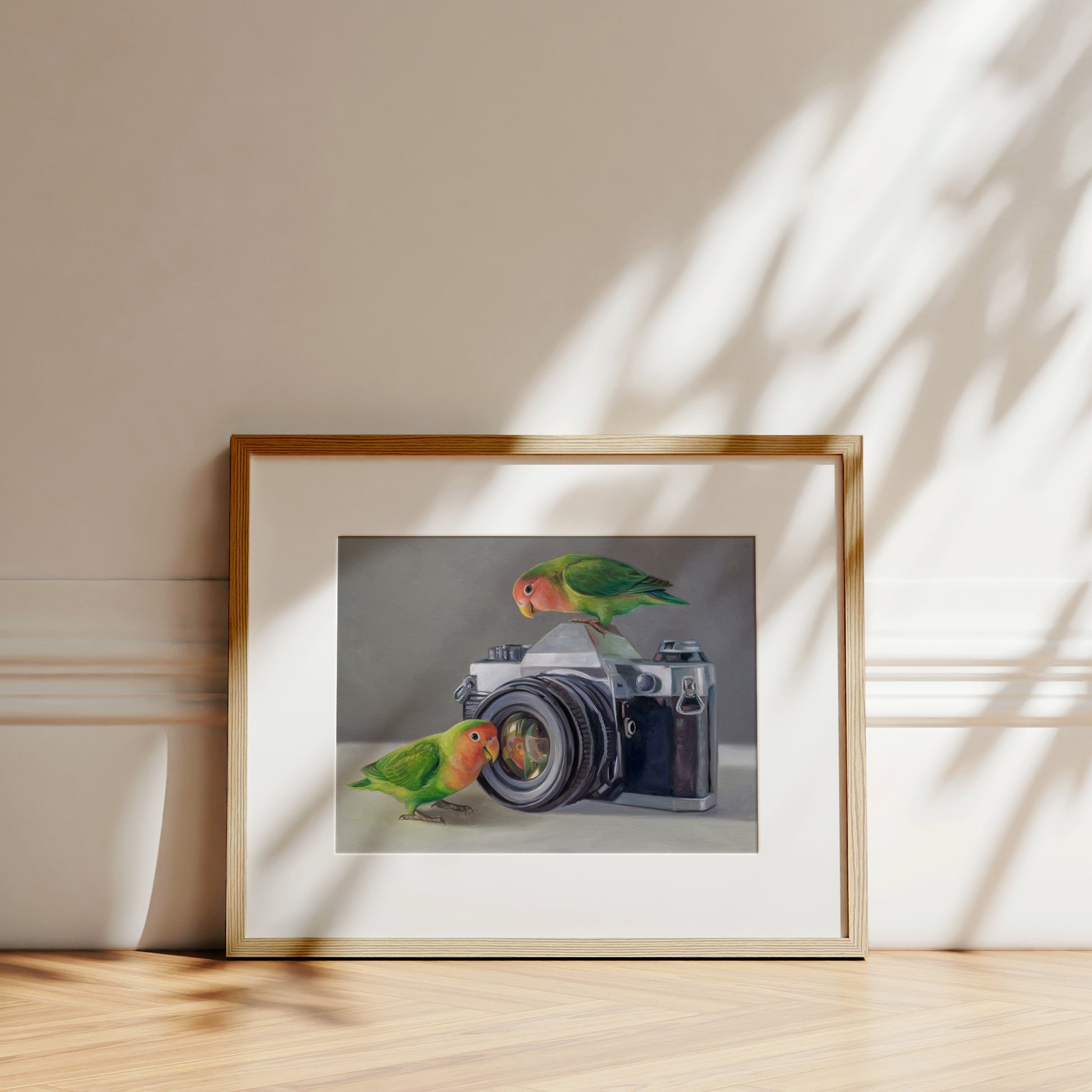 Framed fine art print of two colorful lovebirds on a vintage camera, with a white mat and wood frame.