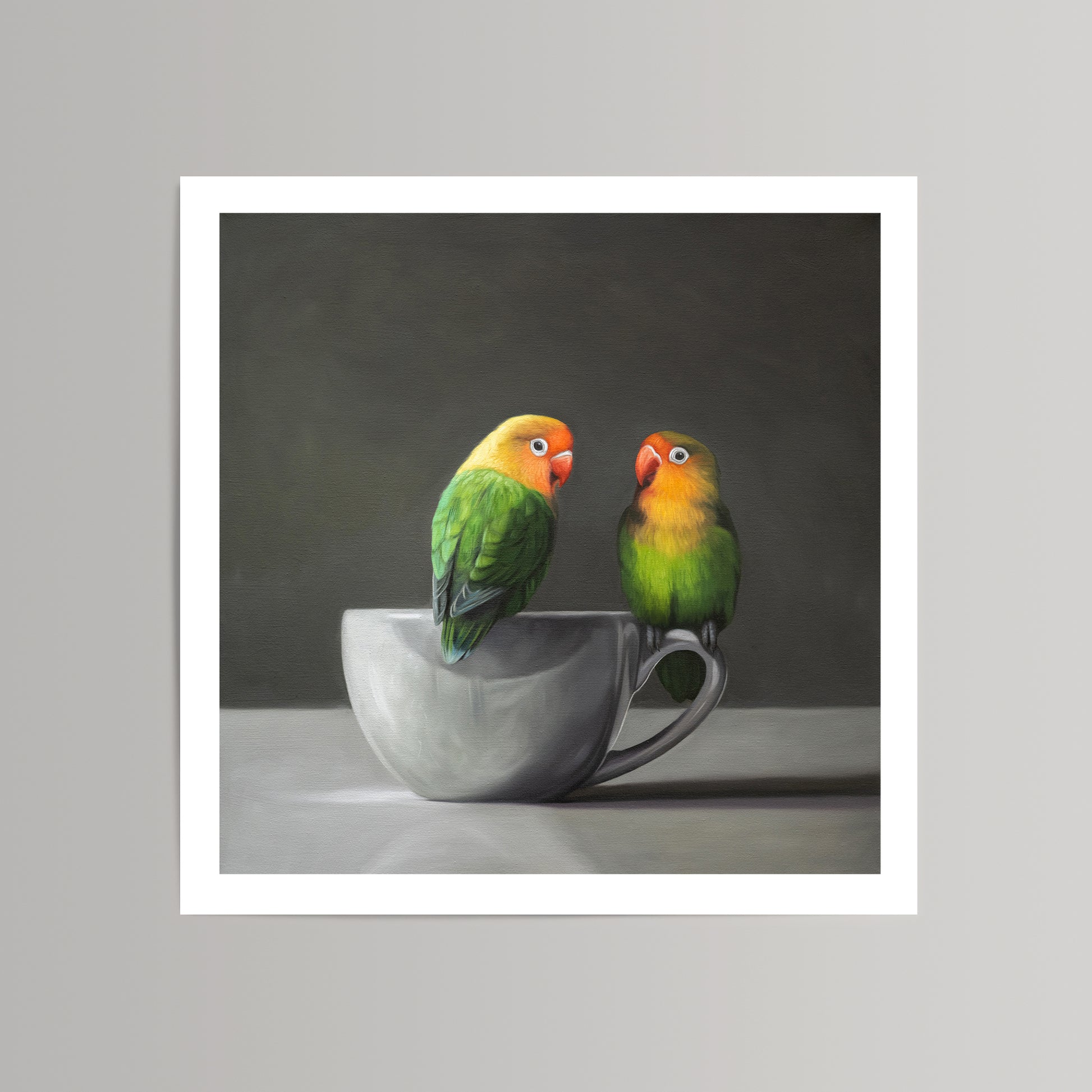 Vibrant fine art print of two green and orange lovebirds perched on a gray porcelain teacup.