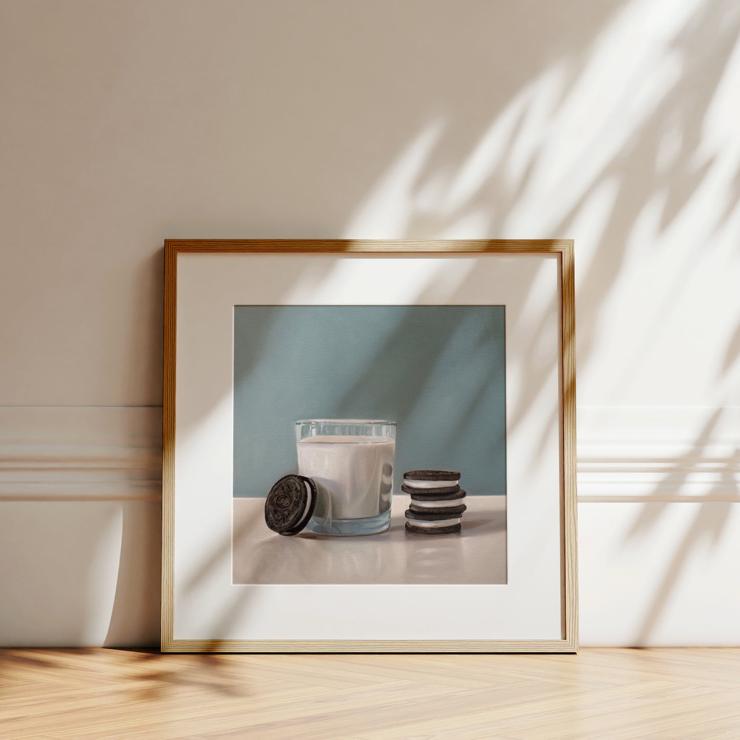 Framed fine art print of a glass of milk with Oreo cookies, featuring a light wood frame and white mat.