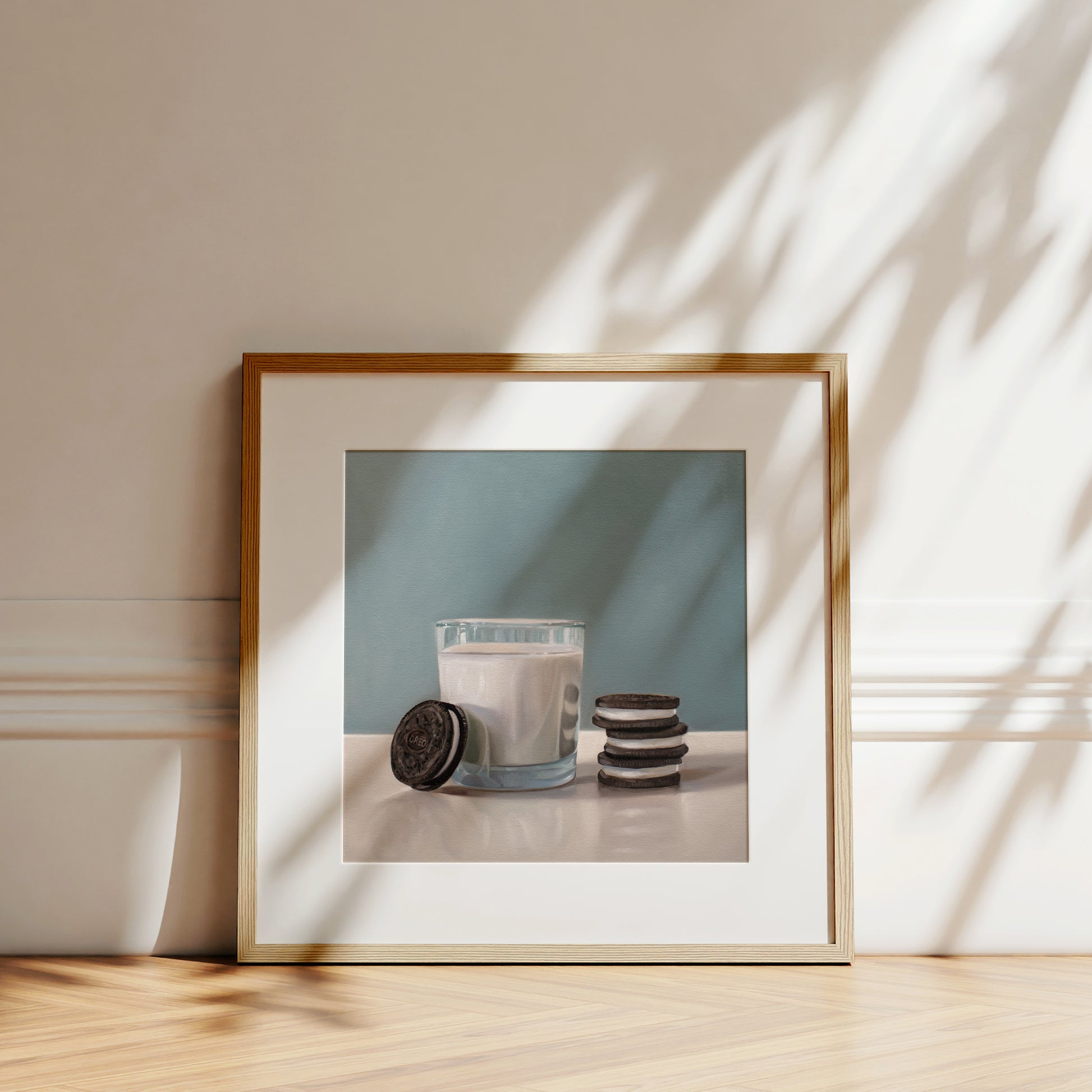 Framed fine art print of a glass of milk with Oreo cookies, featuring a light wood frame and white mat.