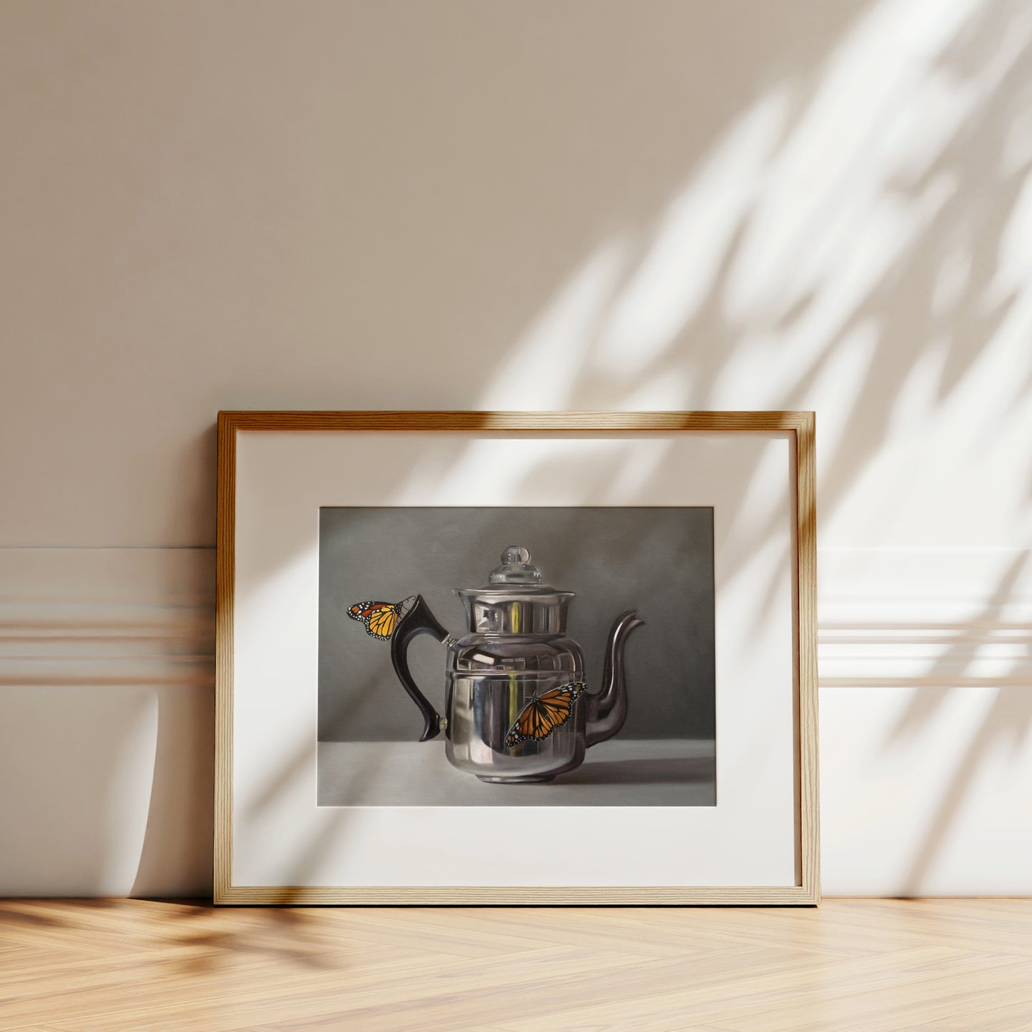 Fine art print of a silver kettle with two orange monarch butterflies, framed in light wood.