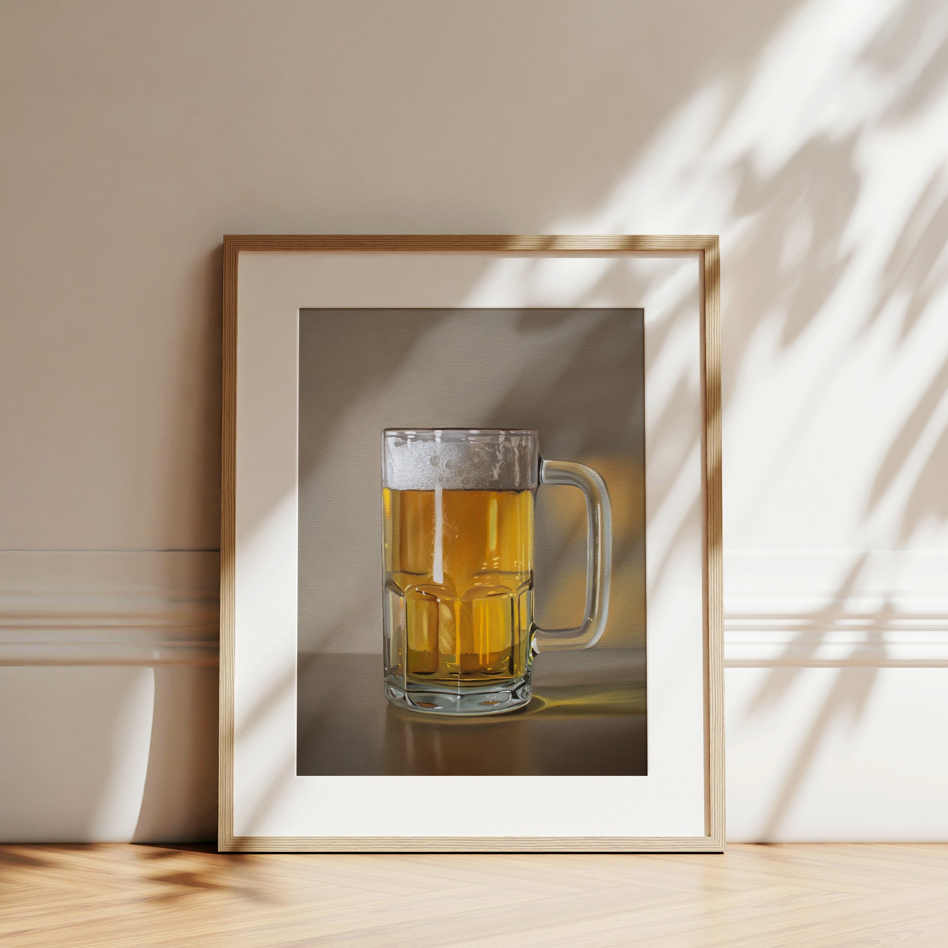 Framed fine art print of a frothy mug of golden beer, leaning against a light wall with sun shadows.
