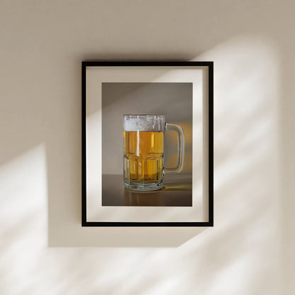 Framed art print of a clear glass mug filled with golden beer and white foam, hanging on a beige wall.