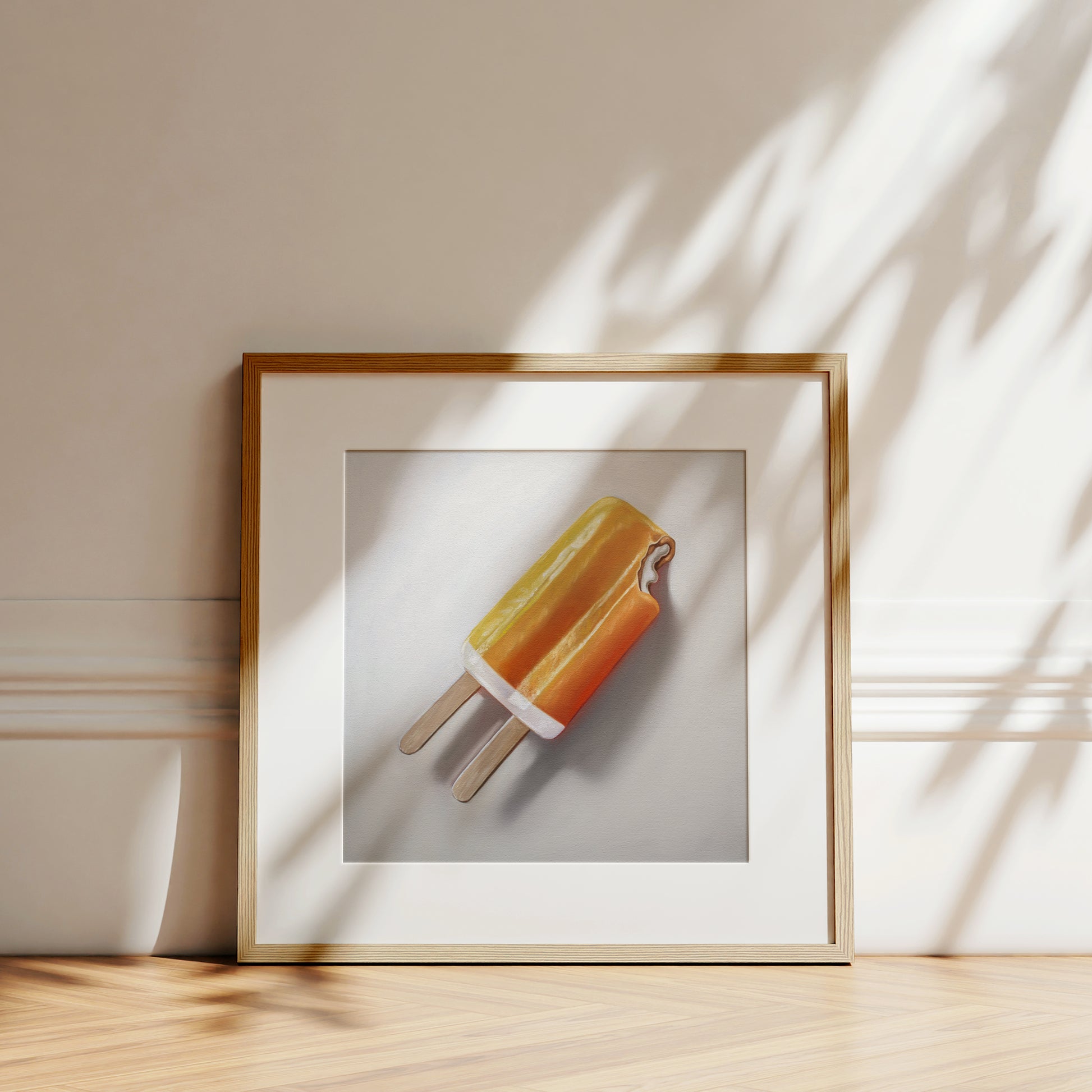 Framed fine art print of an orange dreamsicle on a white background, with a light wood frame.