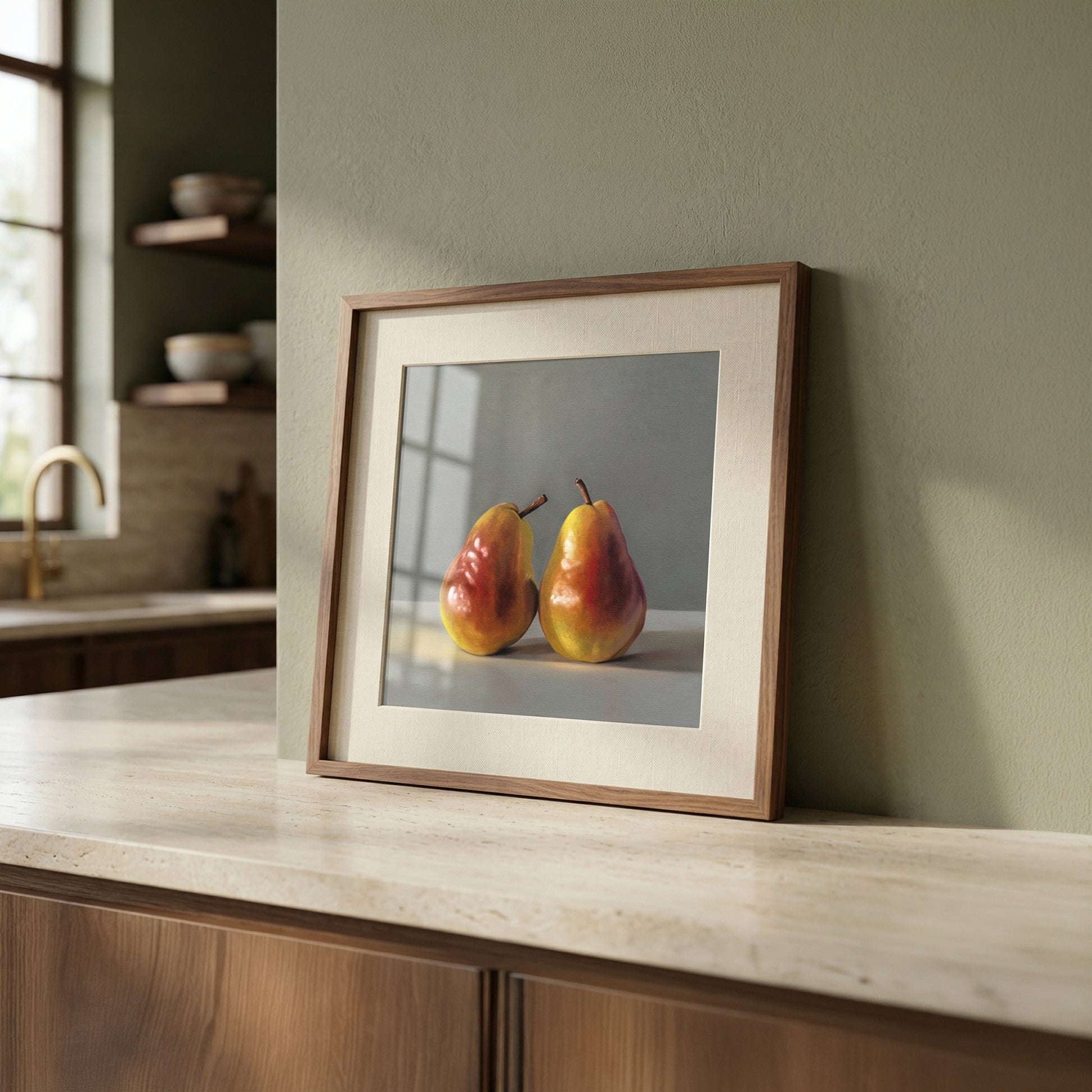 Framed fine art print of two vibrant red and yellow pears, displayed on a light countertop in a modern kitchen.