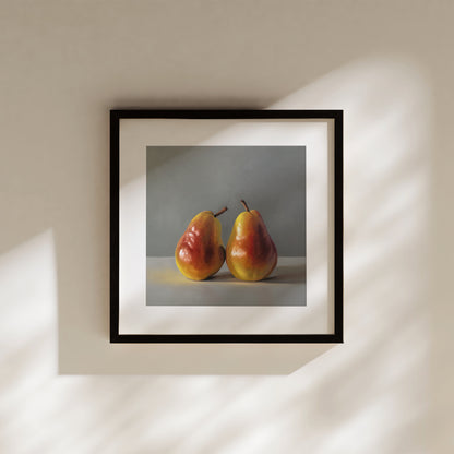 Framed fine art print of two vibrant red and yellow pears on a light surface against a gray background.