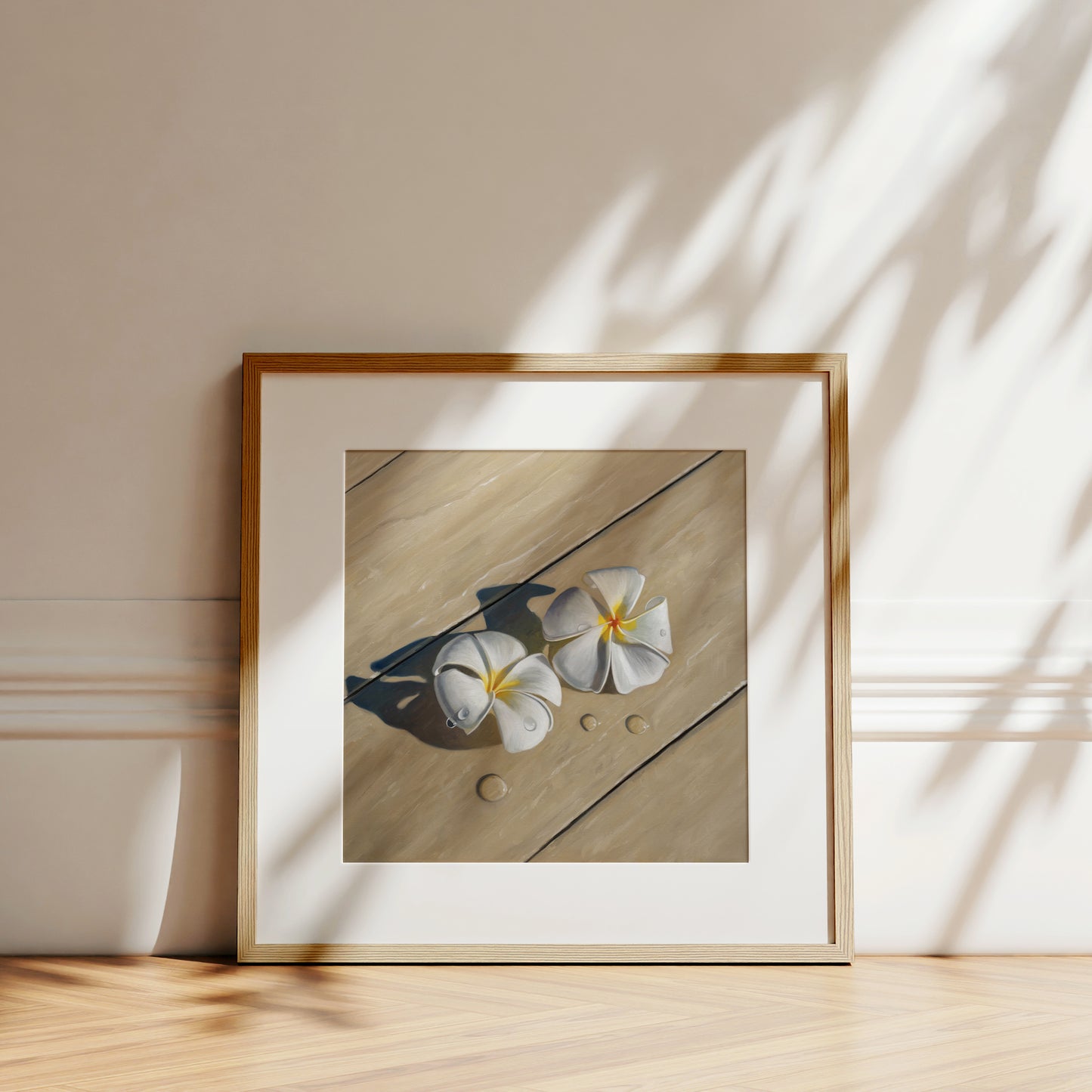 Framed fine art print of two white plumeria flowers with water drops on light wood, leaning against a wall.
