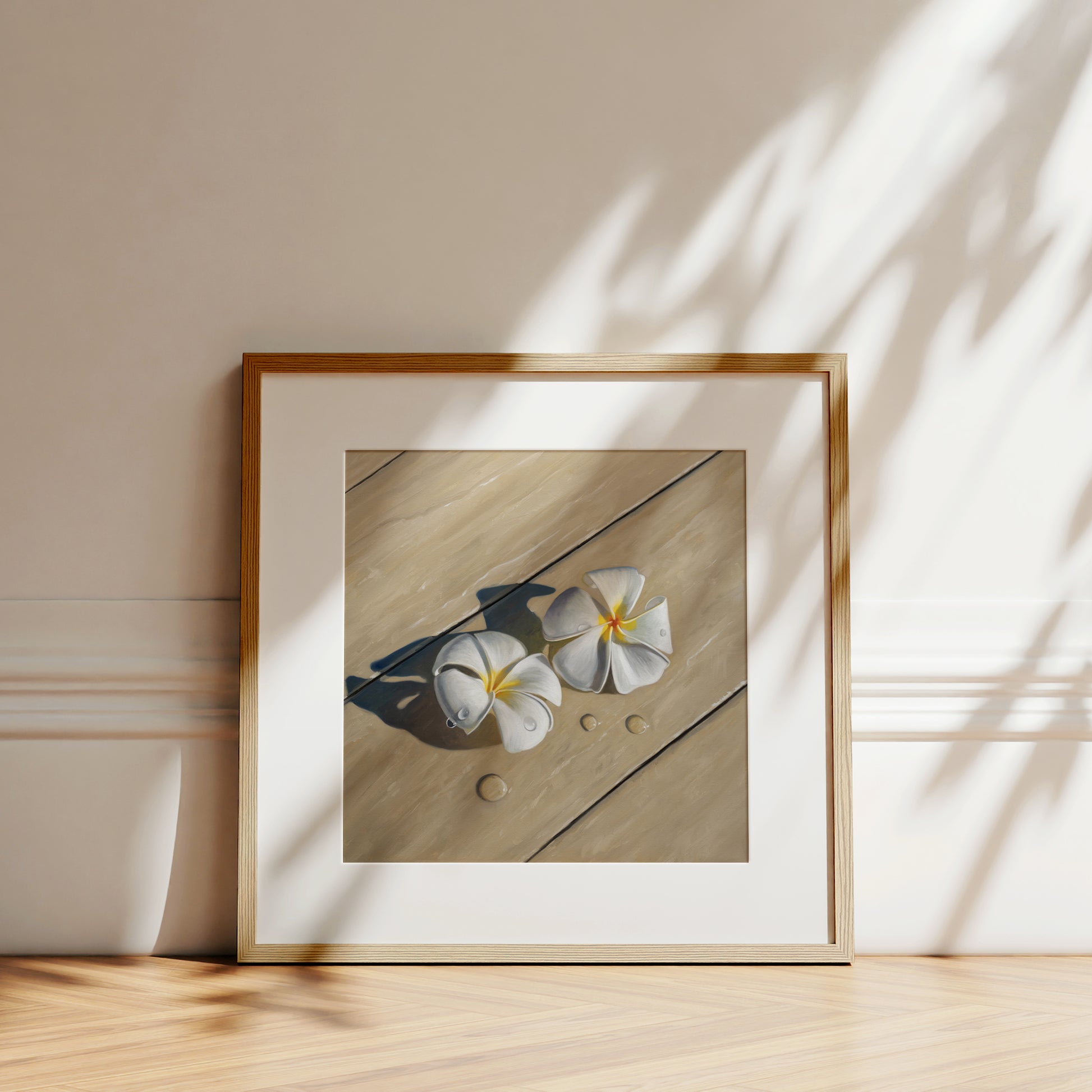 Framed fine art print of two white plumeria flowers with water drops on light wood, leaning against a wall.