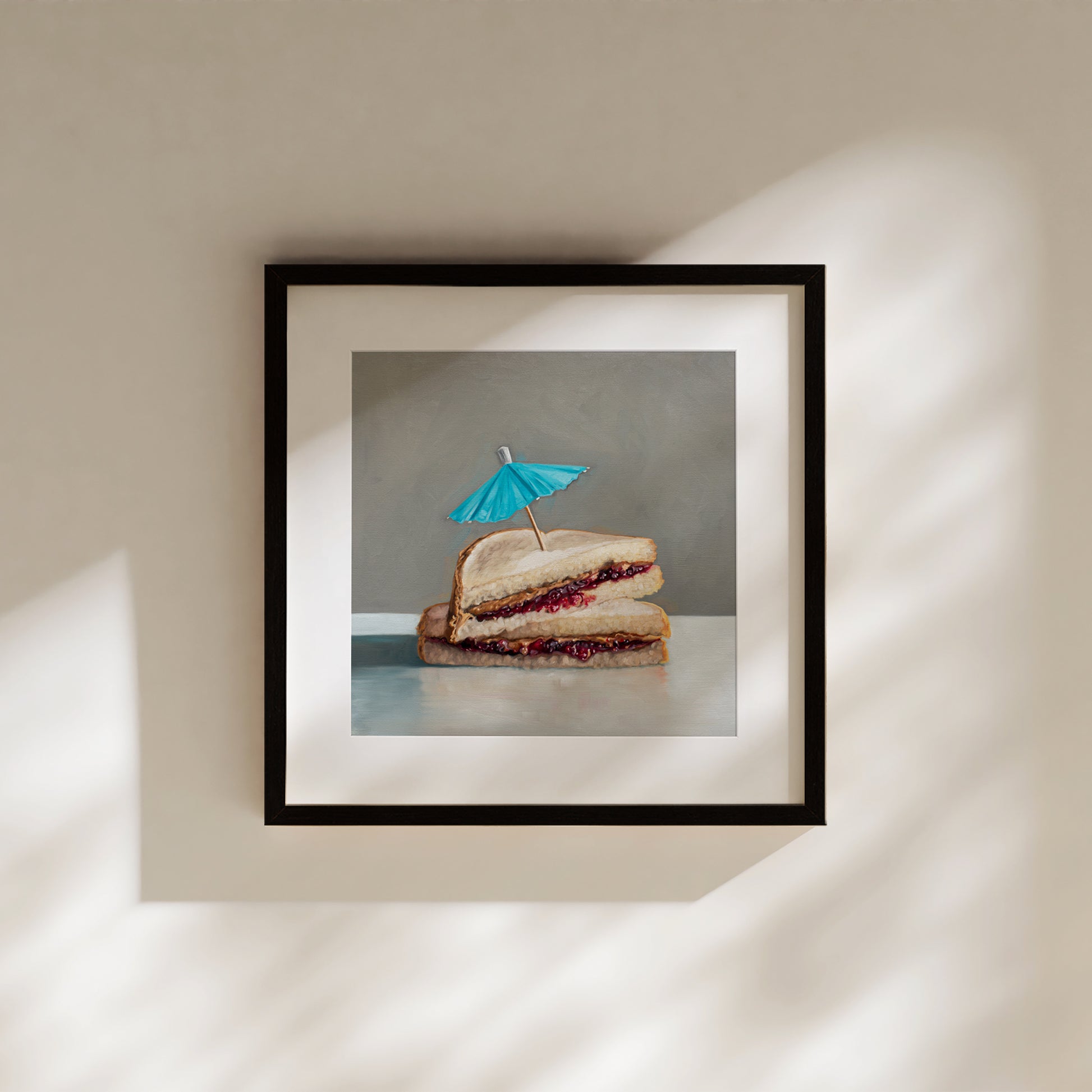 Framed art print of a realistic peanut butter and jelly sandwich with a blue cocktail umbrella.