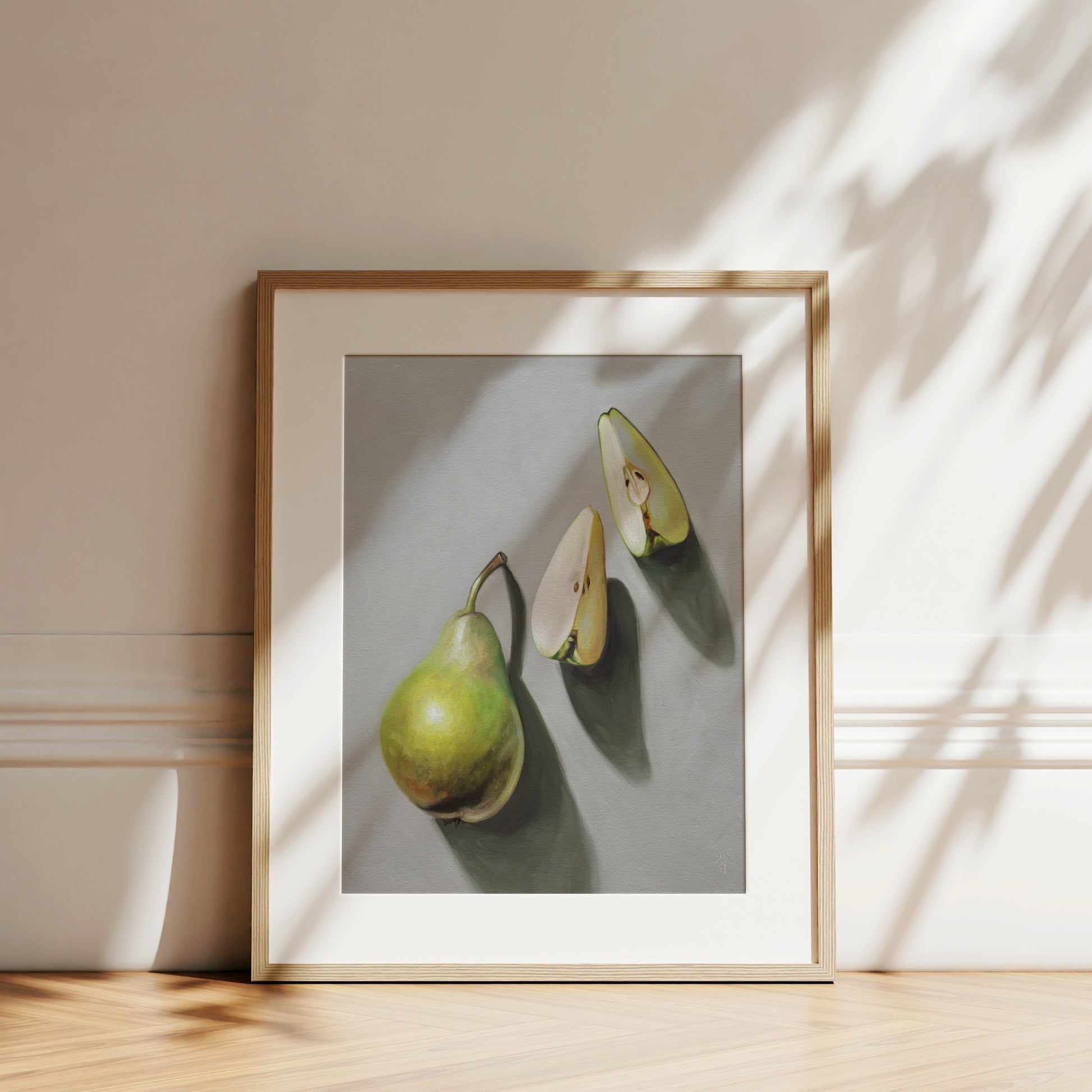 Framed fine art print of a green pear and two pear slices on a gray background, with sunlight shadows.