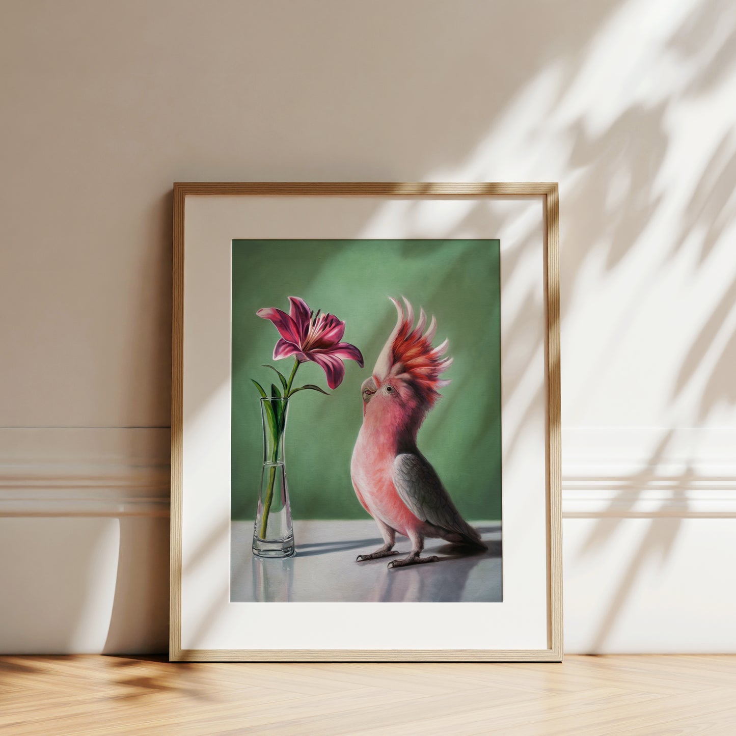 Framed fine art print of a pink cockatoo looking at a deep pink lily in a vase, on a green background.