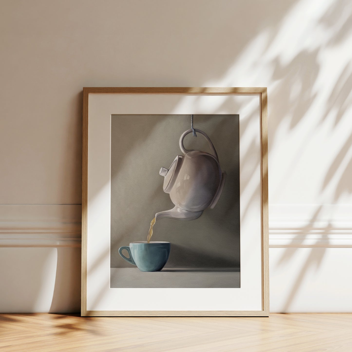 Framed fine art print of a white teapot pouring golden tea into a teal cup, with natural light and shadows.
