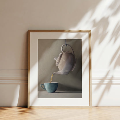Framed fine art print of a white teapot pouring golden tea into a teal cup, with natural light and shadows.