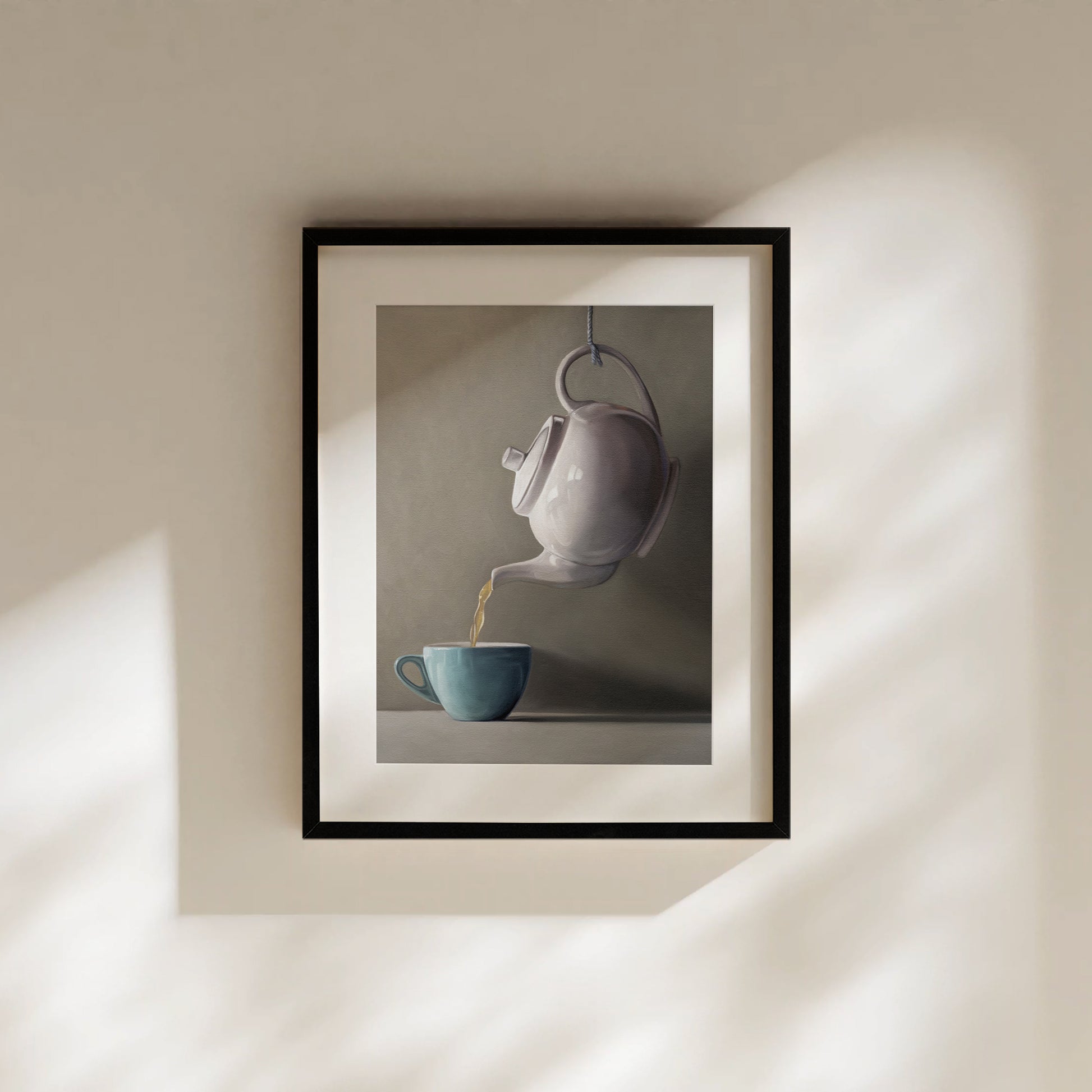 Fine art print of a white teapot pouring golden tea into a teal cup, framed in black.