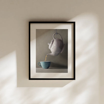 Fine art print of a white teapot pouring golden tea into a teal cup, framed in black.