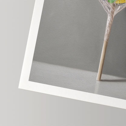 Fine art print of a rainbow swirl lollipop on a stick, wrapped in plastic, with a white border.