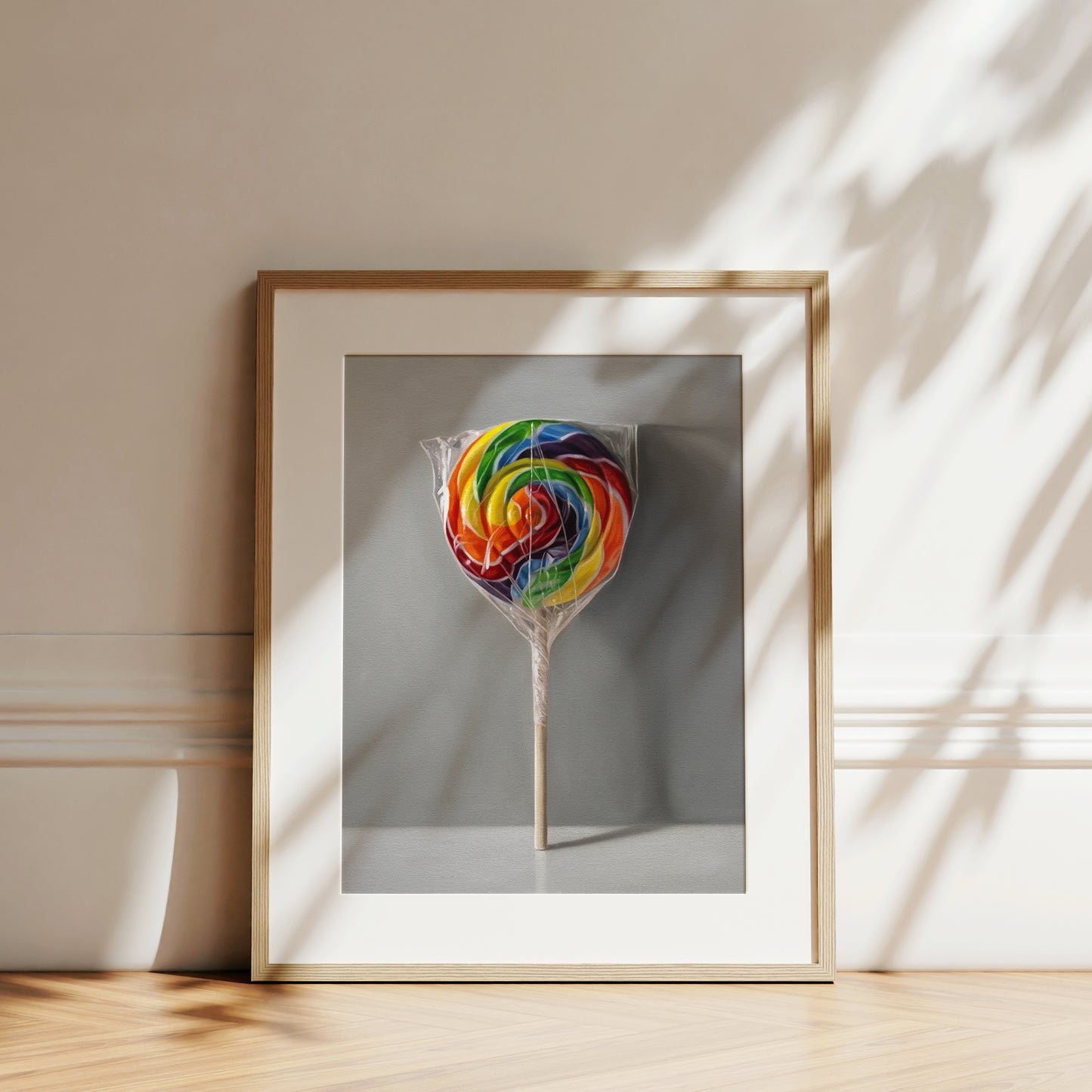 Framed fine art print of a vibrant rainbow swirl lollipop, wrapped in plastic, on a gray background.