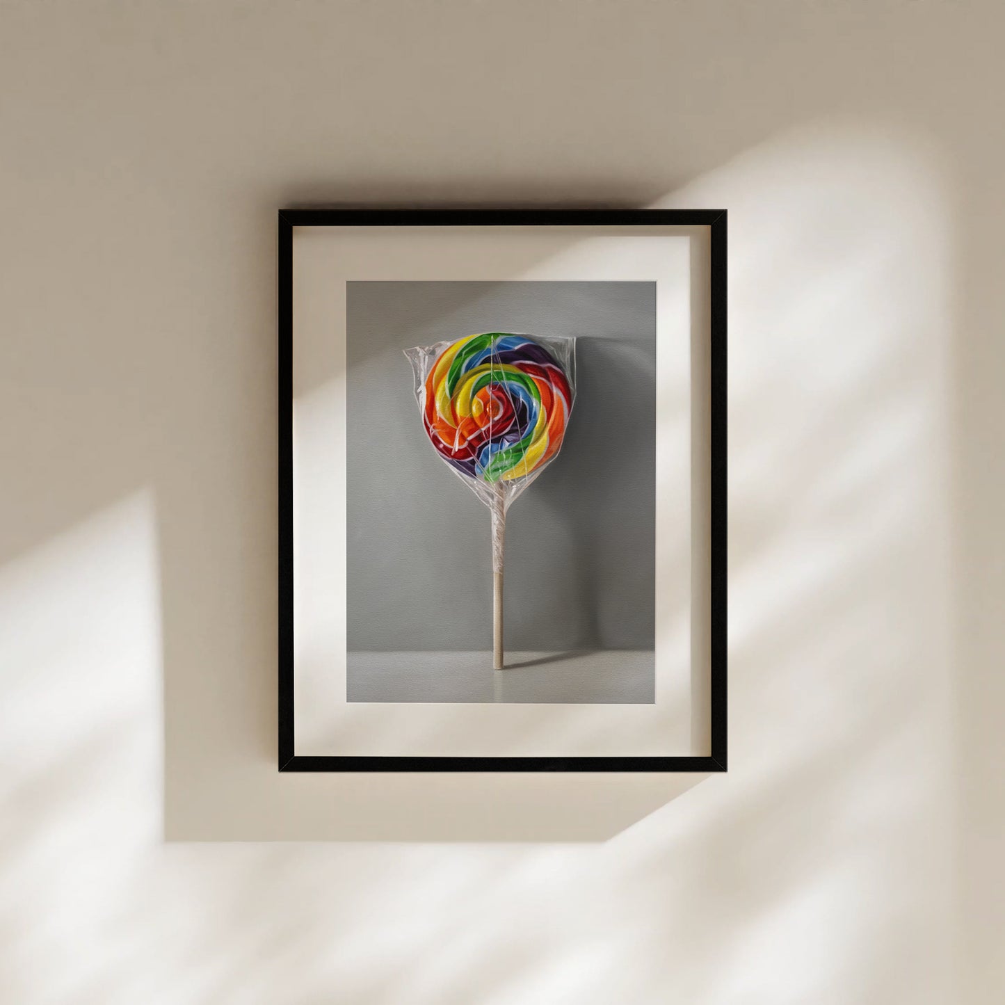 Framed fine art print of a vibrant rainbow swirl lollipop in clear plastic on a light gray background.
