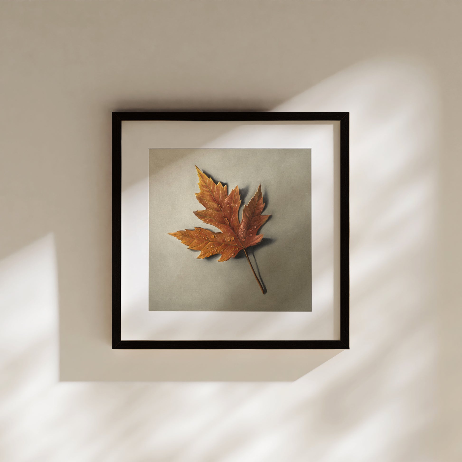 Framed fine art print of a single orange maple leaf with raindrops on a muted background, hanging on a wall.
