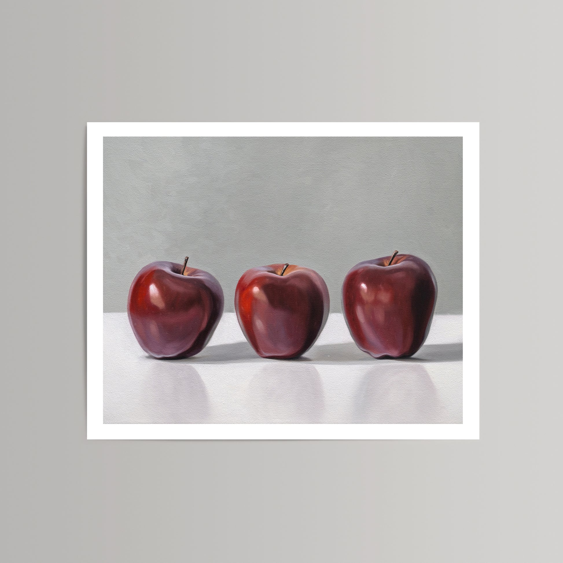 Fine art print featuring three vibrant red apples against a gray background with a white border.