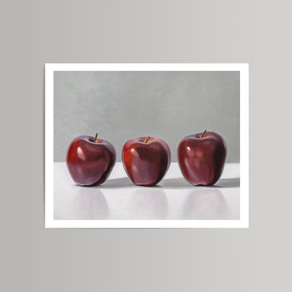 Fine art print featuring three vibrant red apples against a gray background with a white border.