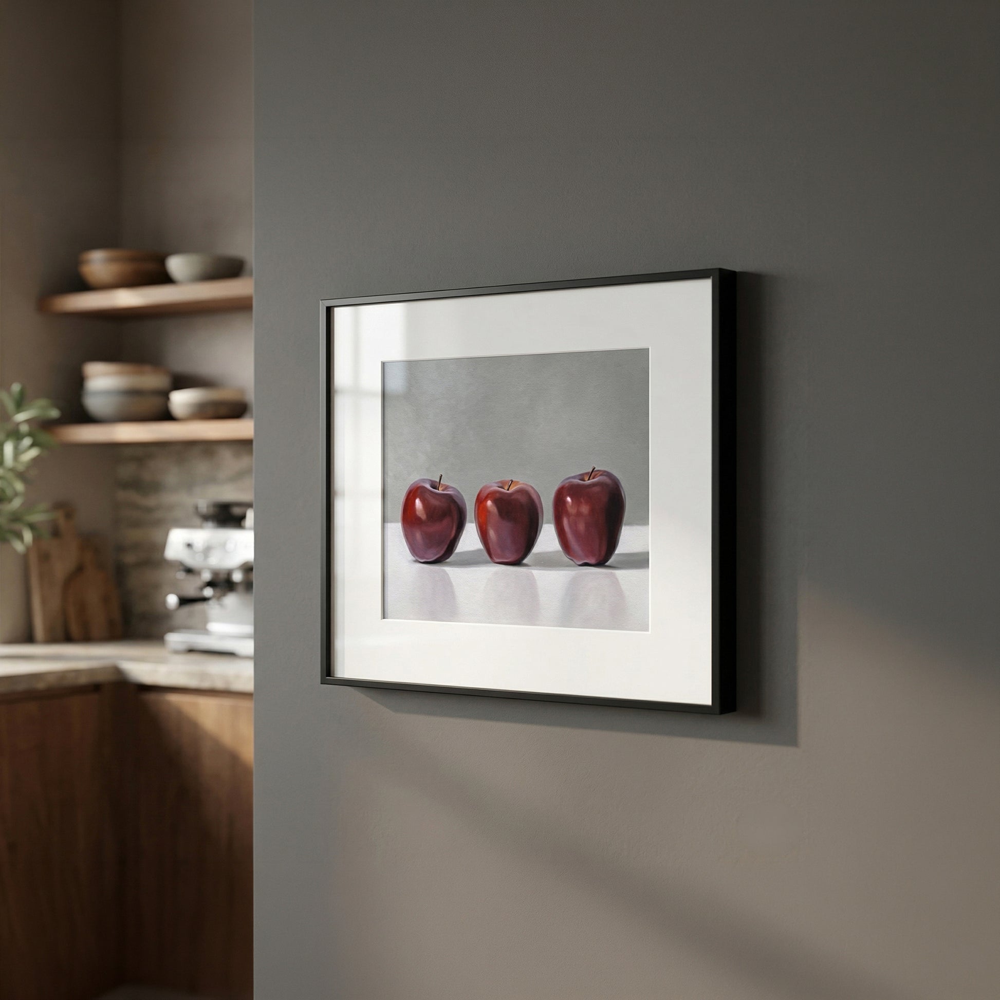 Framed fine art print of three vibrant red apples on a white background, hanging on a dark gray wall.