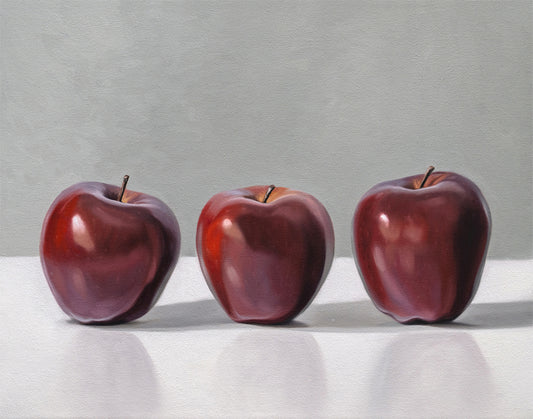 Fine art print of three deep red apples in a row, with subtle reflections on a white surface.