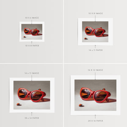 Red Ladies Trio Fine Art Print by Lauren Pretorius: red sunglasses with a reflective surface, two ladybugs on and around them against a neutral background.