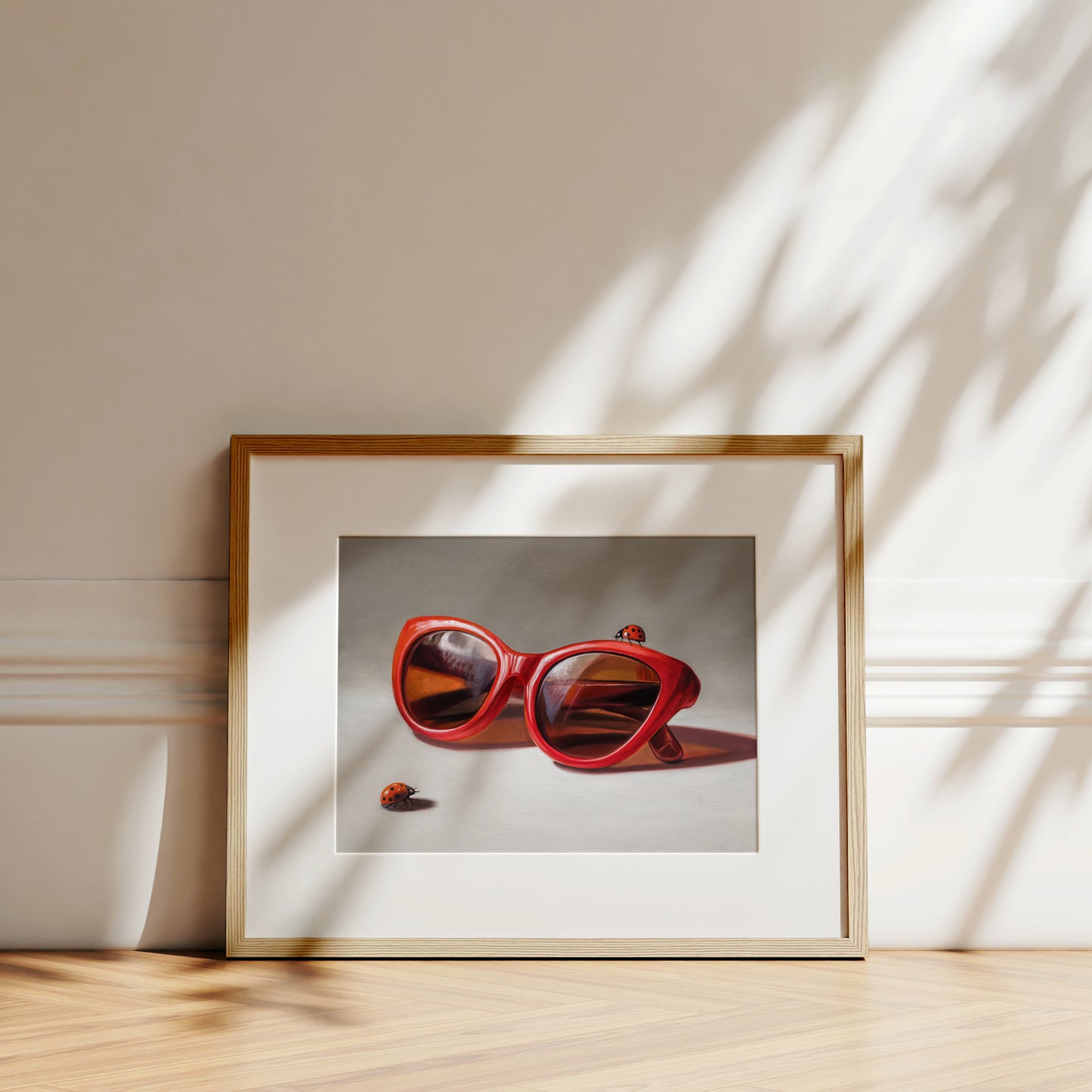 Red Ladies Trio Fine Art Print by Lauren Pretorius: red sunglasses with a reflective surface, two ladybugs on and around them against a neutral background.