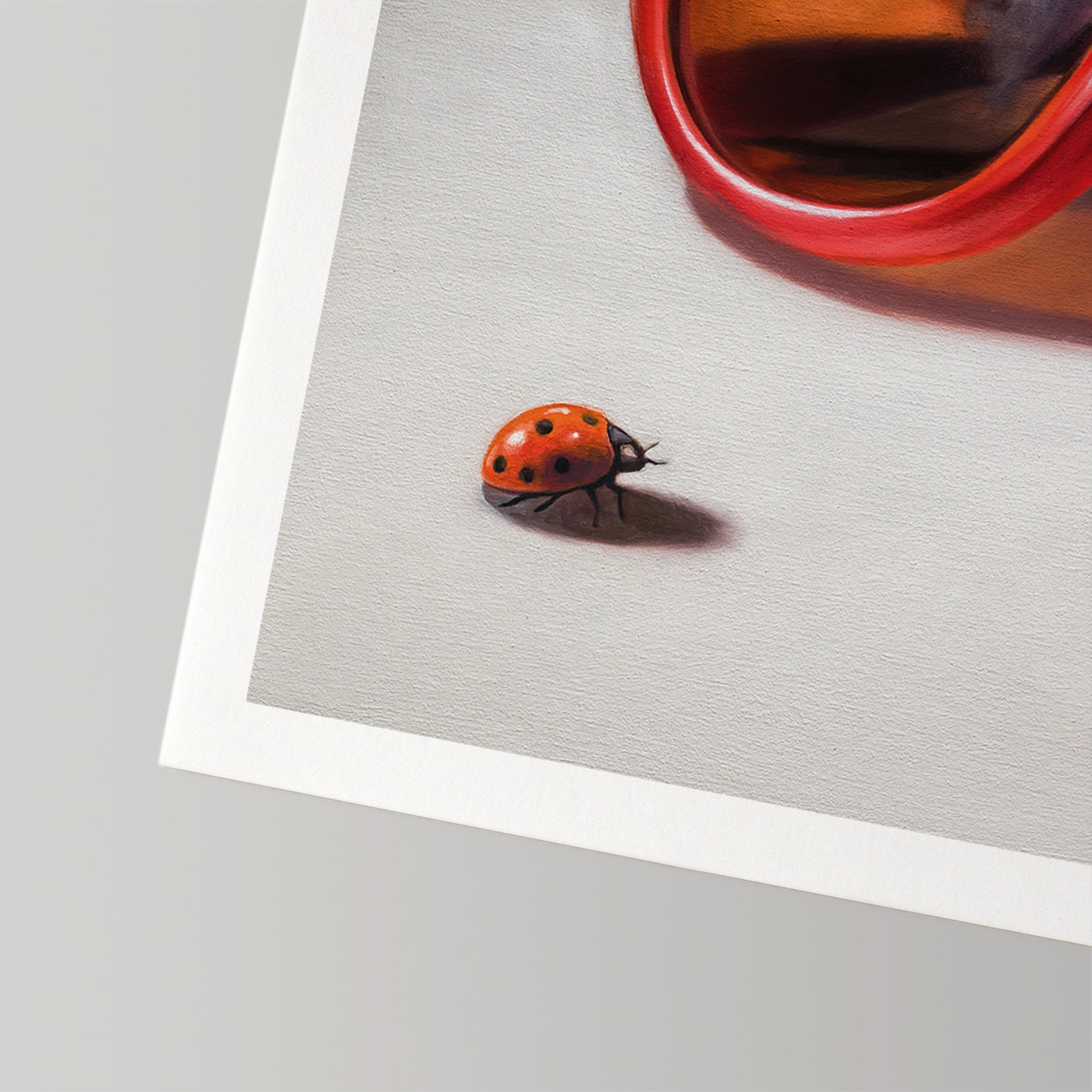 Close-up of a vibrant ladybug on a white fine art print, with a red object partially visible.