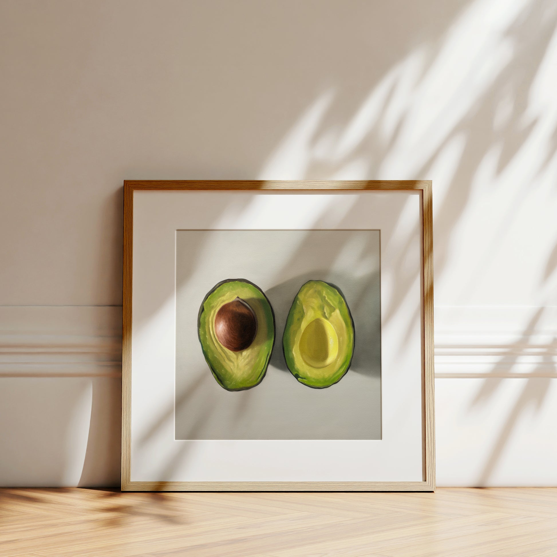 Framed fine art print of two sliced avocados, one with a pit, on a white background.