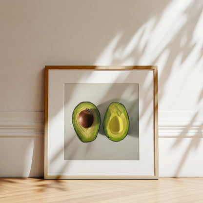Framed fine art print of two sliced avocados, one with a pit, on a white background.