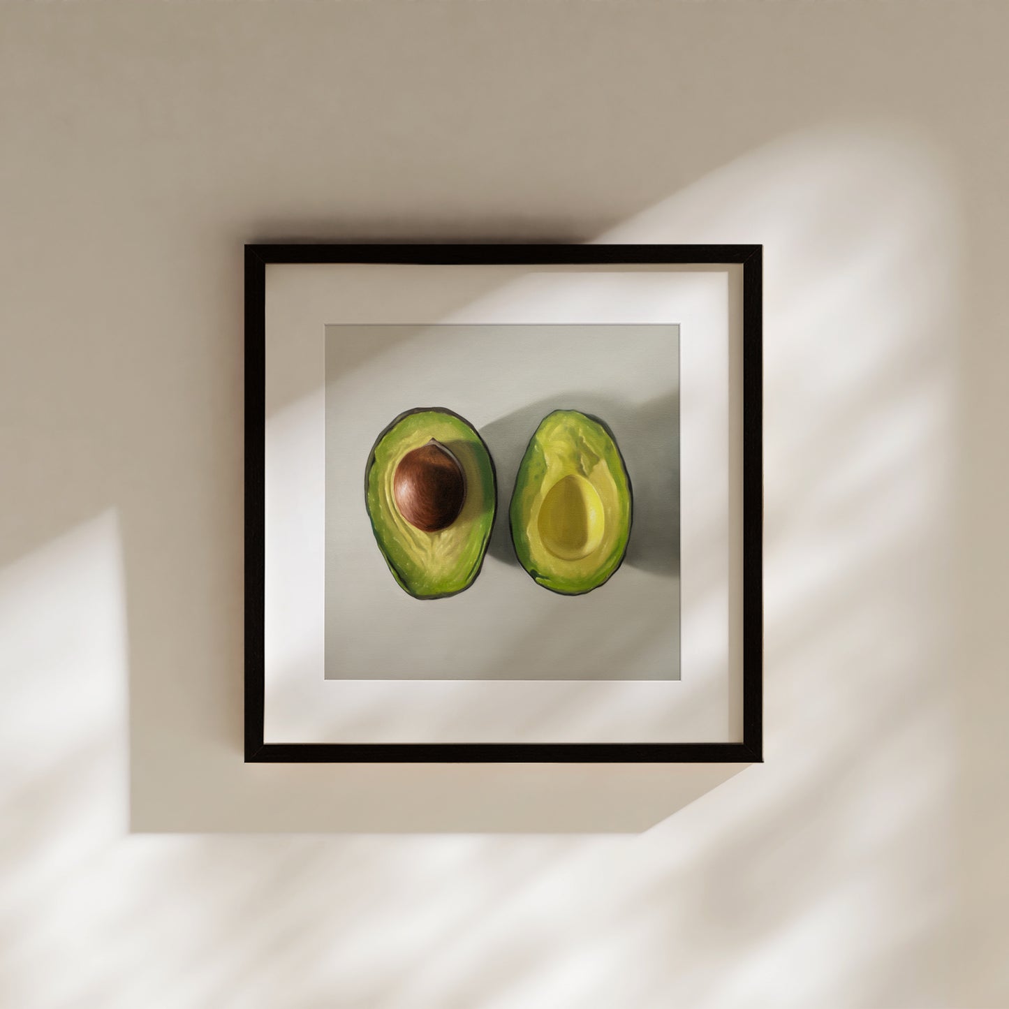 Framed fine art print of two vibrant green avocado halves, one with a brown pit, on a light background.