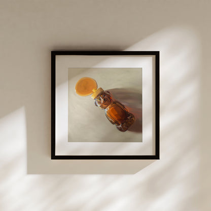 Framed fine art print of a honey bear bottle spilling golden honey, with warm light and shadows.