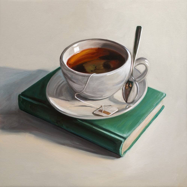 Teacup with saucer and spoon on a green book against a neutral background