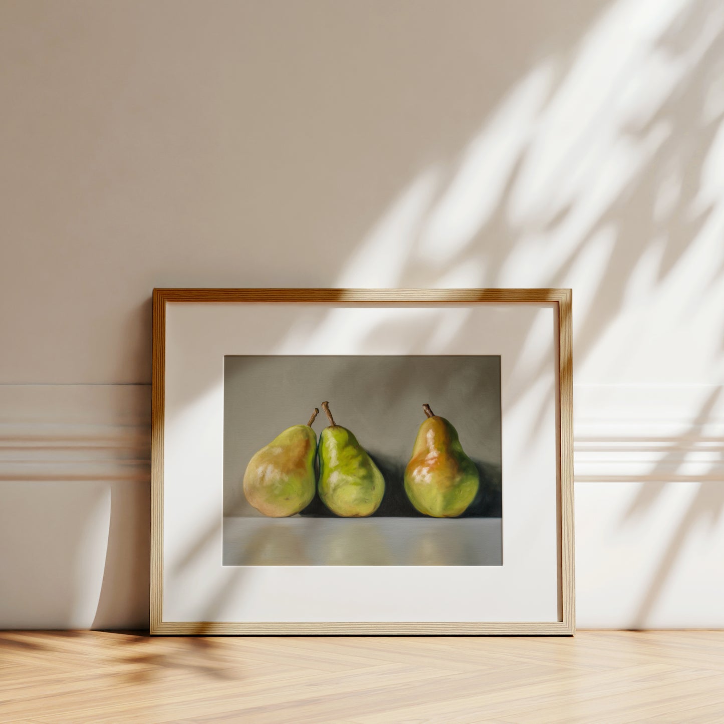 Framed fine art print of three green and yellow pears on a light gray background, leaning against a white wall.